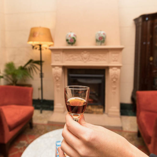 Hand holding small glass of sherry in front of fireplace