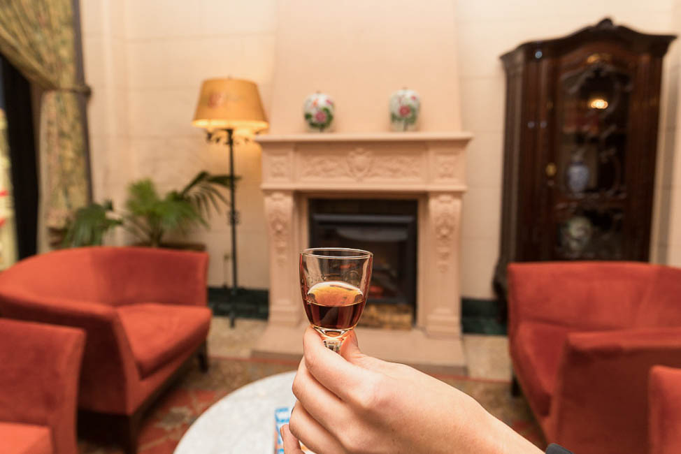 Hand holding small glass of sherry in front of fireplace